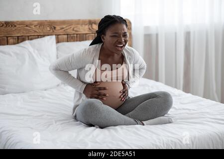 Femme noire enceinte ayant des contractions de travail à la maison, souffrant de mal de ventre Banque D'Images