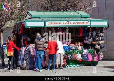 Londres, Royaume-Uni, le 1er avril 2012 : Tourisme achetant un cadeau souvenir dans un marché de rue qui vend des sacs à main en cuir et des accessoires qui ont mangé des voyages populaires Banque D'Images