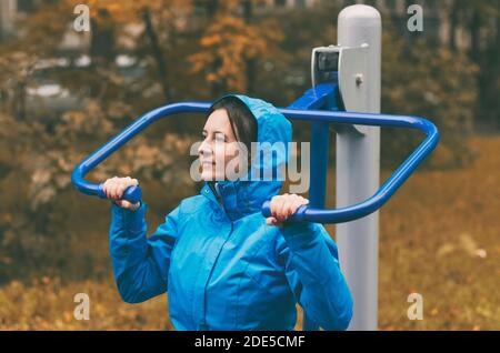 En automne, une jeune femme va pour les sports de plein air se tenir sur les mains courantes d'un simulateur sportif Banque D'Images