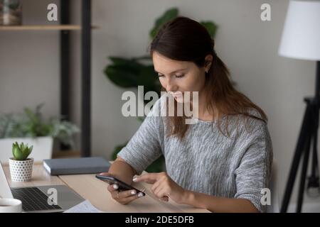 Agréable heureuse femme à cheveux rouges du millénaire utilisant des applications mobiles. Banque D'Images