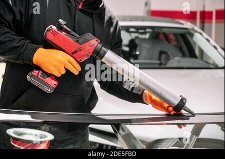 Vitrier appliquant du joint en caoutchouc sur le pare-brise dans le garage, gros plan. Photo de haute qualité Banque D'Images