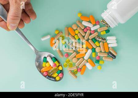 les médicaments colorés ont été déversés de la boîte et une main tenant une grande cuillère pleine de pilules. Banque D'Images