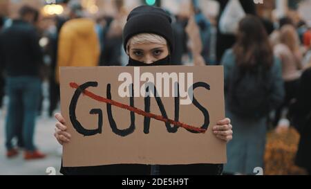 Pas de pistolets. Jeune femme avec masque facial tenant une bannière contre la violence d'armes à feu. Démonstration et concept de révolution. Photo de haute qualité Banque D'Images