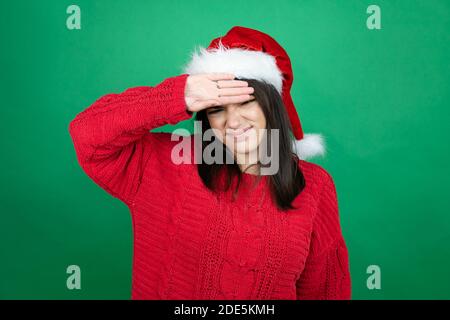 Jeune belle femme portant chapeau de Noël Santa sur fond vert isolé touchant le front pour la maladie et la fièvre, la grippe et le froid, virus malade Banque D'Images