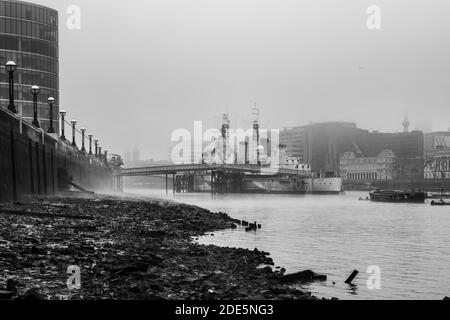 Le HMS Belfast Royal Navy noir et blanc s'est amarré à la Tamise à marée basse depuis une plage de la Tamise à Londres par temps brumeux, tourné dans le cadre du confinement du coronavirus Covid-19 en Angleterre, en Europe Banque D'Images