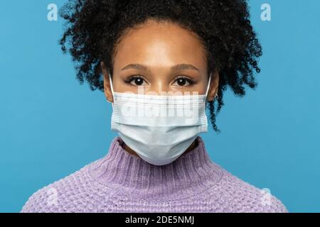 Gros plan portrait en studio de femme afro-américaine porter un masque médical pendant le covid-19, l'épidémie de coronavirus ou la saison de la grippe, isolée sur le backgroun bleu Banque D'Images