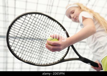 Main de jeune fille blonde en blanc activewear tenant le tennis jouez sous la raquette tout en vous apprêtant à jouer devant vous de caméra au stade Banque D'Images