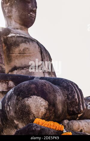 Grande statue de Bouddha en pierre, main droite sur le genou vers la terre, bouddhiste offrant des fleurs orange marigold dans la guirlande. Premier plan ciblé Banque D'Images