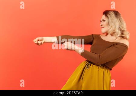 Vue latérale portrait d'une femme ambitieuse forte en blouse brune prétendant tirer la corde invisible, concept de travail dur, effort et les efforts pour réaliser Banque D'Images