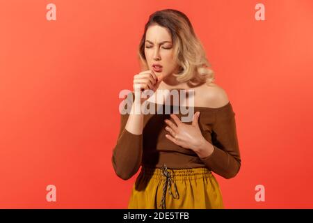 Portrait d'une jeune femme adulte malade aux cheveux blonds bouclés toux et sensation de douleur dans ses poumons. Symptômes de la maladie. Prise de vue en studio en intérieur isolée o Banque D'Images