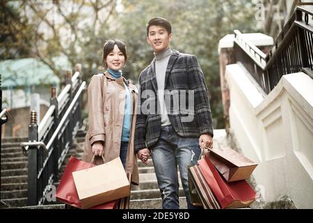 portrait en plein air d'un jeune couple asiatique heureux debout sur des marches avec des sacs à provisions en papier à portée de main Banque D'Images