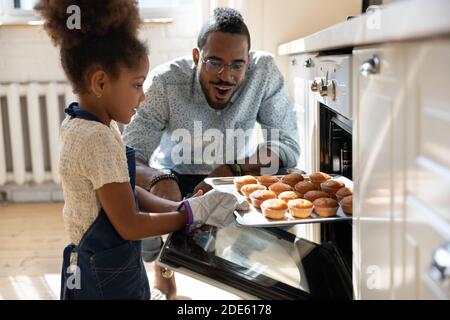 Un père africain enthousiaste regardant sa fille sortir des muffins du four Banque D'Images