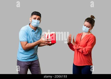 Portrait de l'homme mécontent avec masque médical chirurgical donnant présent à une femme mécontente, fille mécontente montrant geste de refus, mauvais cadeau. isola Banque D'Images