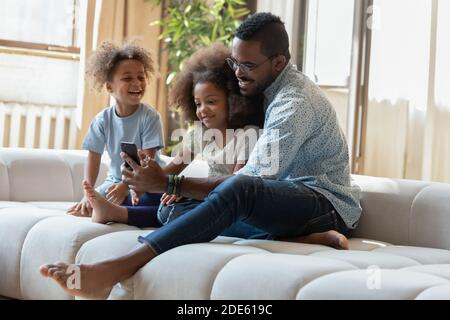 Un père africain et deux enfants regardent des dessins humoristiques sur un téléphone portable Banque D'Images