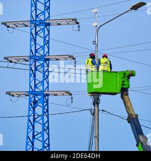 Électriciens en uniforme réparant les fils électriques sur un pôle haut Banque D'Images