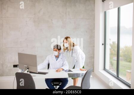 Médecins de couple avec des masques médicaux de protection du visage parlant et utilisation de l'ordinateur dans l'image Banque D'Images