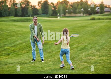 Joyeux père jouant au badminton avec sa petite fille joyeuse à l'extérieur dans le parc, un jour d'été Banque D'Images