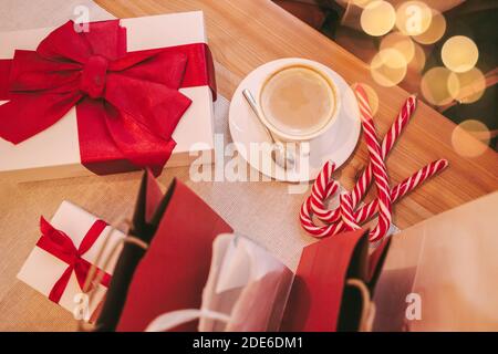 Vue de dessus d'une tasse à café, boîtes-cadeaux avec noeud rouge et sacs de shopping sur une table en bois au restaurant. Cadeaux et sacs en papier pour la fête du nouvel an. Hiver Banque D'Images