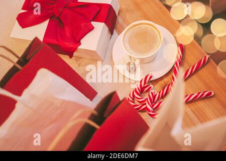 Vue de dessus des boîtes-cadeaux de fête de Noël et des sacs en papier sur une table en bois dans le café. Présente avec ruban rouge, café, bonbons de canne, sacs à provisions. Banque D'Images