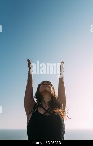 Image verticale d'une jeune femme mince vêtue de noir et levant les bras au ciel. Concept de yoga. Copier l'espace Banque D'Images