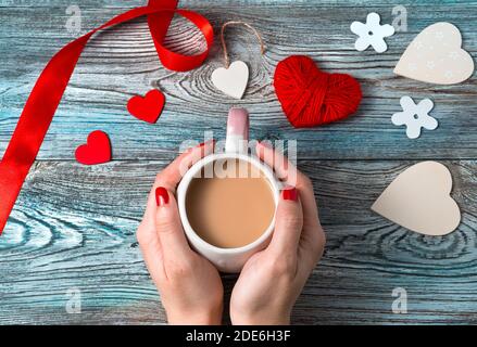 Mains d'une femme tenant une tasse de café avec du lait sur un fond romantique. Banque D'Images