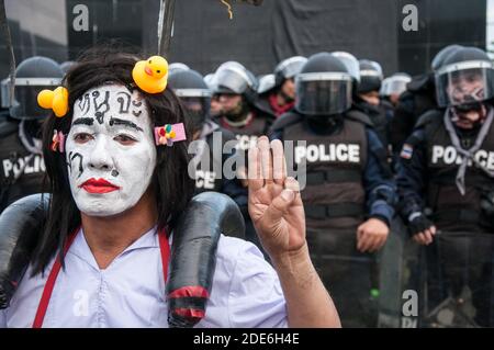 Un manifestant avec un visage peint rendant hommage aux trois doigts devant les policiers anti-émeutes pendant la manifestation. Des milliers de manifestants pro-démocratie se sont rassemblés au BTS wat phra si mahathe où ils ont défilé au 11e Régiment d'infanterie (la garde du roi) pour s'opposer à la législation visant à contrôler certaines unités de l'armée par le roi Maha Vajiralongkorn et pour appeler à des réformes de la monarchie. Banque D'Images