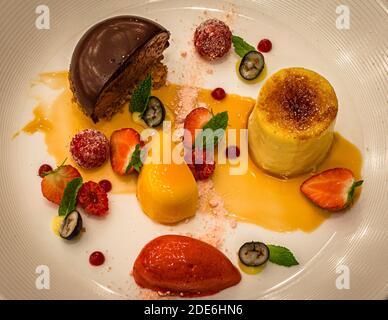 Assiette de dessert avec un dôme de mousse au chocolat, crème brûlée, sorbet à la mangue et à la fraise, framboises sucrées, et fraises et myrtilles fraîches avec gel citronné, servi au restaurant « The Grill » du The Dunloe Hotel & Gardens au Gap of Dunloe près de Killarney, comté de Kerry, Irlande. Le chef Jupp Osterloh dirige la cuisine de l’hôtel depuis plus de 25 ans. Banque D'Images