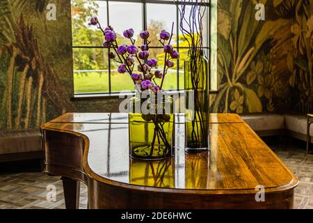 Un piano à queue Steinway contient deux vases en verre vert avec des branches de coton séchées au Dunloe Hotel & Gardens, un hôtel cinq étoiles près de Killarney, dans le comté de Kerry, en Irlande. Un papier peint botanique avec de grands motifs de feuilles et une vue sur le jardin encadrent la scène. Banque D'Images