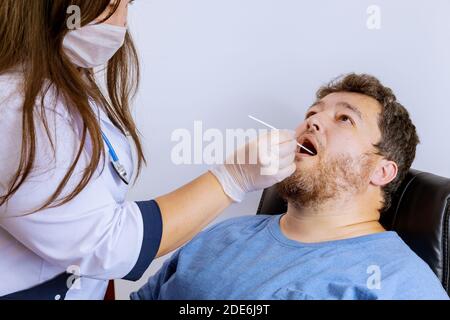 Un travailleur de la santé qui a de l'équipement effectue un écouvillon de coronavirus sur un écouvillon de bouche d'homme pour le coronavirus COVID-19. Banque D'Images