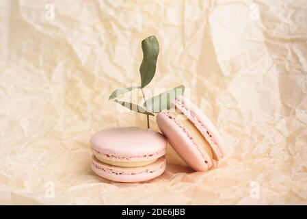 Deux savoureux macarons de couleur jaune-français et eucalyptus sur fond de papier froissé beige. Macarons colorés. Vue avant. Banque D'Images