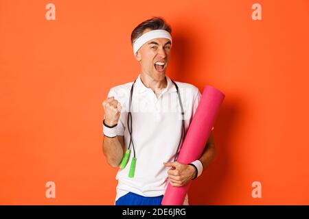 Concept d'entraînement, de gym et de style de vie. Image d'un homme de forme physique d'âge moyen motivé et heureux, atteindre l'objectif, dire oui et faire la pompe poing, tenue Banque D'Images