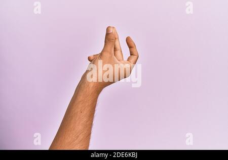 Bras et main du jeune homme caucasien sur fond rose isolé se prenant les doigts pour le succès, facile et clic symbole geste avec la main Banque D'Images