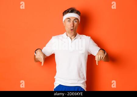 Concept d'entraînement, de sport et de style de vie. Portrait d'un athlète masculin d'âge moyen surpris, portant des vêtements pour la salle de sport, pointant les doigts vers le bas et regardant Banque D'Images
