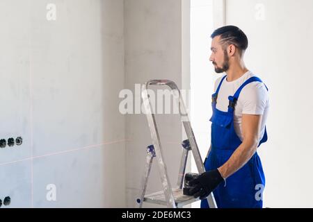 Le handyman a mis le niveau laser sur l'échelle et regarde les marques sur le mur Banque D'Images