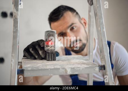 L'homme a mis le niveau sur une échelle et regarde aux relevés de l'appareil Banque D'Images