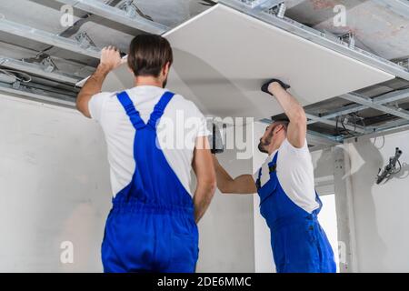 Les contremaîtres en combinaison bleue se tiennent sur une échelle et font un plafond Banque D'Images