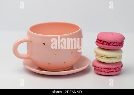 Macarons à côté d'une tasse rose. Isolé sur fond blanc. Macarons colorés faits maison de style français Banque D'Images