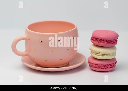 Macarons à côté d'une tasse rose. Isolé sur fond blanc. Macarons colorés faits maison de style français Banque D'Images
