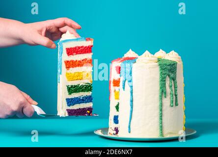 Les mains de la femme prennent une tranche de gâteau arc-en-ciel. Délicieux gâteau d'anniversaire maison sur fond bleu. Banque D'Images