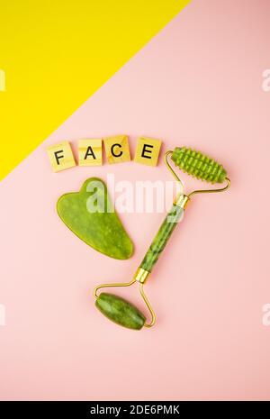 Outils de massage facial Gua Sha Green. Rouleau en jade de quartz vert sur fond rose-jaune. La face d'inscription en lettres de bois Banque D'Images