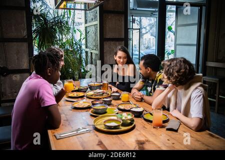 Un groupe multiculturel de jeunes dans un café, manger de la nourriture asiatique, boire des cocktails, discuter. Banque D'Images