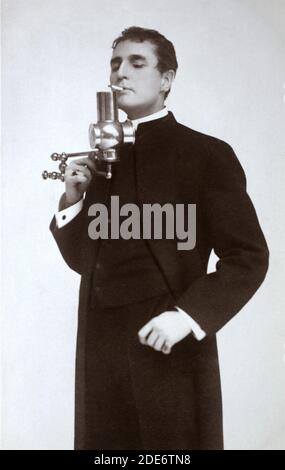 Le célèbre acteur, directeur, dramaturge et scénariste américain William Gillette (1853 – 1937) a posé en costume Sherlock Holmes, éclairant une cigarette d'une lampe. Prise d'une carte postale photographique de l'époque. Banque D'Images