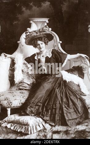 La célèbre actrice et chanteuse anglaise édouardienne Lily Elsie (1886 – 1962) assise avec un chapeau et une robe noirs, tirée d'une carte postale photographique de l'époque. Banque D'Images