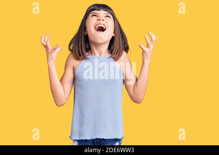 Jeune fille avec bang portant des vêtements décontractés fou et fou criant et hurlant avec l'expression agressive et les bras levés. Concept de frustration. Banque D'Images