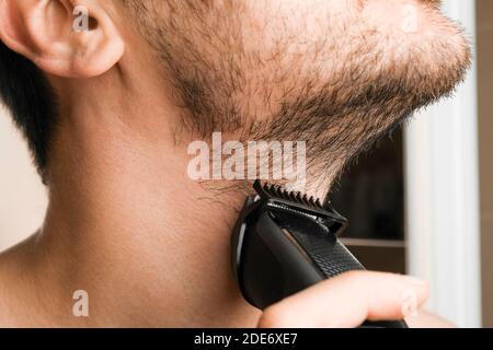 Homme rasant la barbe et le cou avec un rasoir électrique. Routine du matin. Tonte de la barbe avec une tondeuse. Banque D'Images