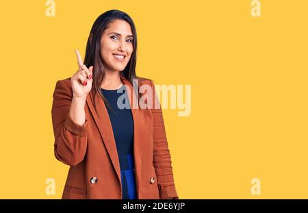 Jeune belle brune femme portant des vêtements élégants montrant et pointant vers le haut avec le doigt numéro un tout en souriant confiant et heureux. Banque D'Images