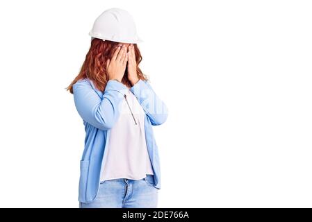 Jeune femme latine portant un casque d'architecte avec une triste expression couvrant le visage avec les mains en pleurant. Concept de dépression. Banque D'Images