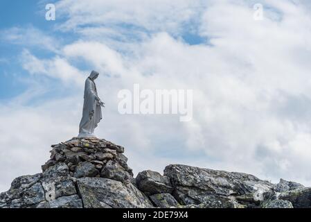 Statue blanche de la Vierge Marie, mère de Dieu, placée au sommet de la montagne. En arrière-plan, il y a des sommets enneigés de hautes montagnes, ciel bleu. Banque D'Images