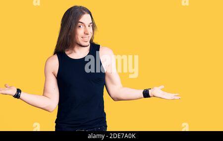Jeune homme adulte avec de longs cheveux portant le style goth avec des vêtements noirs souriant montrant les deux mains ouvertes paumes, présentation et publicité comparaison et Banque D'Images