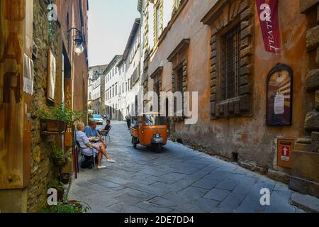 Ruelle étroite dans le centre historique de la vieille ville étrusque avec des gens au café-trottoir et une petite voiture de passage APE Piaggio, Volterra, Toscane, Italie Banque D'Images